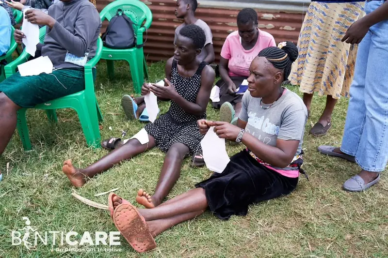 Women and girls sitting on the grass sewing reusable sanitary pads during a training session