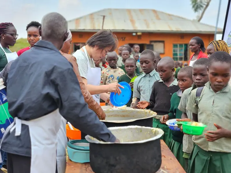 Volunteers and staff serving a meal from large pots to children at a BintiCare feeding day