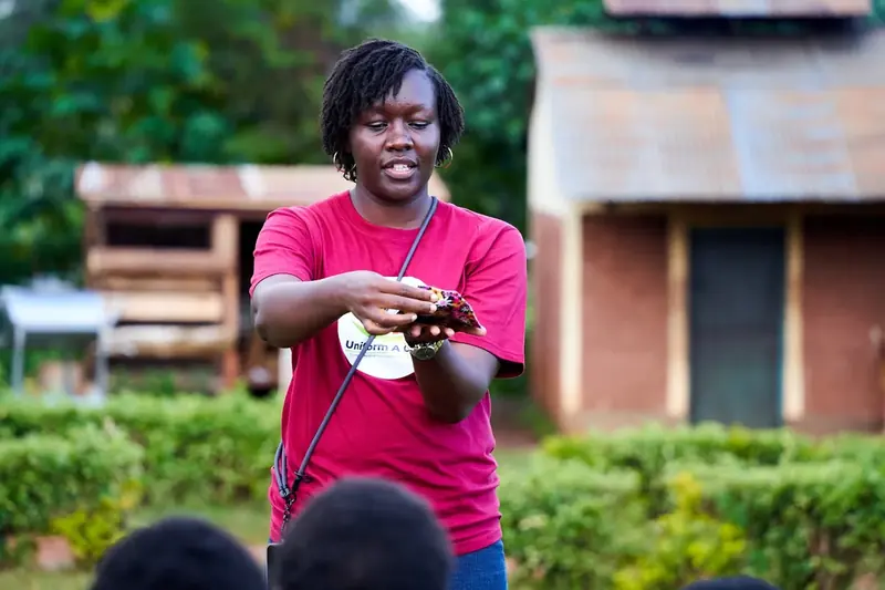 A trainer in a magenta t-shirt demonstrating a reusable sanitary pad to a school audience