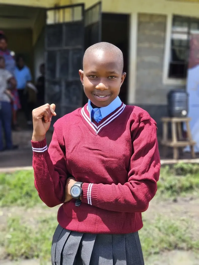 A learner in a maroon sweater and new school uniform standing confidently outdoors